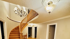 Ein großzügiger Innenraum mit einer Holztreppe, die zu einer zweiten Etage führt, einer Kristallleuchtre und einer strukturierten Decke.