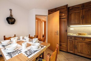 Ein Essbereich mit Tisch für vier Personen, Holzschränken und einer Küchenzeile mit einem Korb auf der Arbeitsfläche.