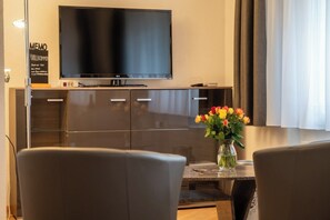 Ein modernes Wohnzimmer mit Flachbildfernseher, einem Esstisch mit Stühlen und einer Blumenvase.