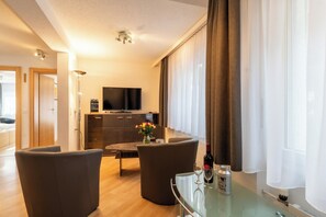 Un salon moderne avec un téléviseur à écran plat, une table basse en verre et deux fauteuils.