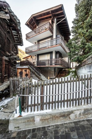 Un immeuble à plusieurs étages doté de balcons, d’une clôture en bois et d’un escalier en pierre menant à l’entrée.