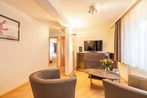 Ein modernes Wohnzimmer mit Essbereich, einem Fernseher und einer Küche im Hintergrund.