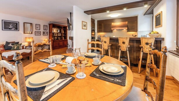 Un coin repas avec une table ronde dressée pour quatre personnes, entourée de chaises en bois ornées de motifs sculptés.