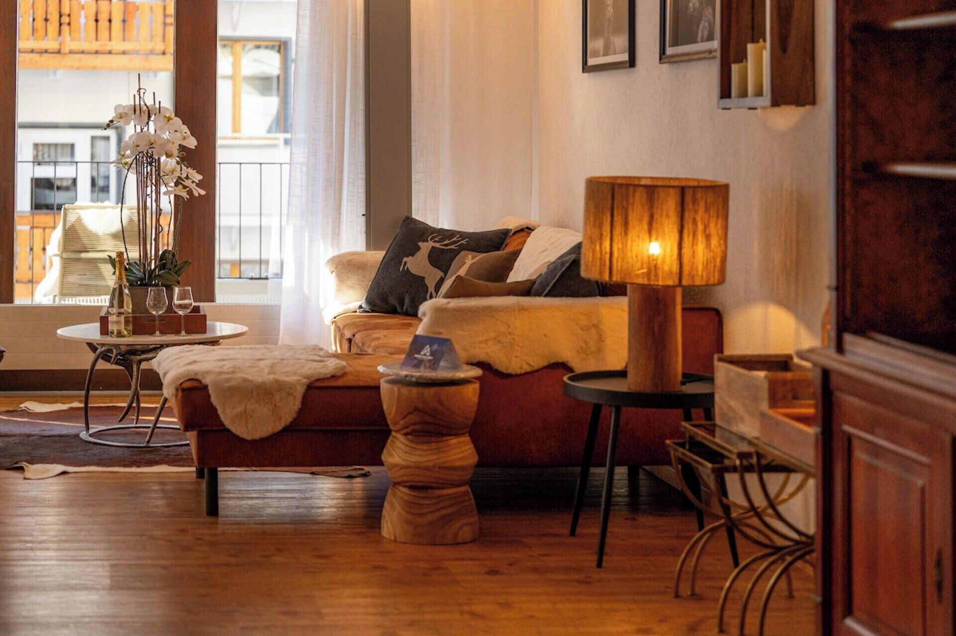 A cozy living room with a sofa, a lamp, a small table with a bottle and glasses, and a decorative plant.