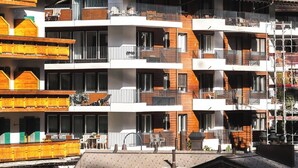 Un hôtel à plusieurs étages doté de balcons, avec une piste de ski en arrière-plan et un paysage montagneux.