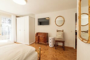 Ein Schlafzimmer mit einem Bett, einem Schminktisch, einem Sessel, einem Fernseher und einem Spiegel.
