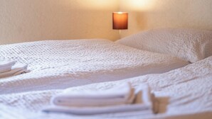 A neatly made bed with a white blanket and pillows, a wall-mounted lamp, and folded towels on the bed. - Serene Alpine Luxury in Zermatt 1089 (Wallis)