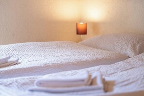 Ein ordentlich bezogenes Bett mit weißer Decke und Kissen, eine Wandlampe und gefaltete Handtücher auf dem Bett.