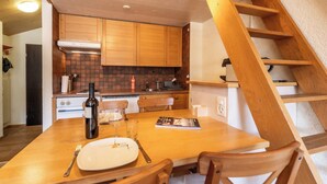A wooden dining table with a plate, cutlery, and a bottle. A wooden staircase is visible to the right. - Serene Alpine Luxury in Zermatt 1089 (Wallis)