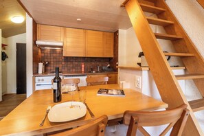 Ein Holztisch mit einem Teller, Besteck und einer Flasche. Eine Holztreppe ist rechts im Bild zu sehen.