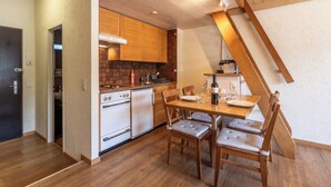 A compact kitchen with wooden cabinets, a dining table with chairs, and a staircase. - Serene Alpine Luxury in Zermatt 1089 (Wallis)