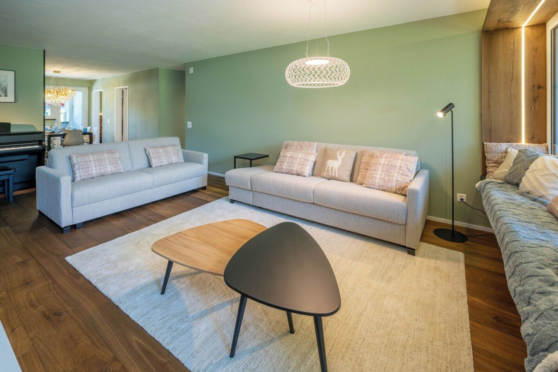A living room with two sofas, a coffee table, a floor lamp, and a piano in the background.