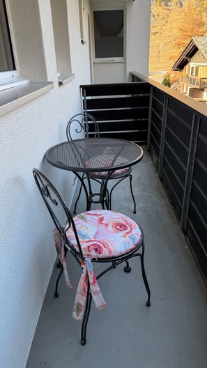 Ein Balkon mit einem runden Metalltisch und zwei Stühlen, einer davon mit einem Blumenkissen.