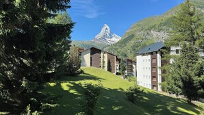 A residential area with modern buildings, a grassy hill, and a mountain in the background. - Alpine Elegance with Matterhorn Views 1083 (Wallis)