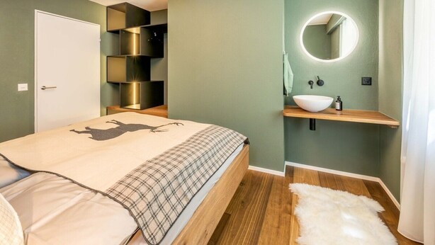 A bedroom with a bed, a bedside table, a mirror, a shelf, and a door. - Alpine Elegance with Matterhorn Views 1083 (Wallis)