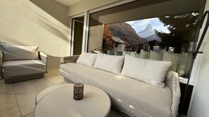 A modern living room with a sofa, a coffee table, and a view of a mountain landscape through a large window. - Alpine Elegance with Matterhorn Views 1083 (Wallis)