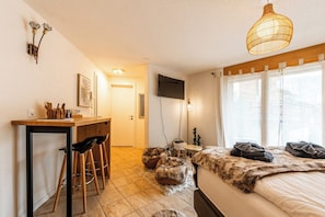 Ein Schlafzimmer mit einem Bett, einem Schreibtisch mit Stühlen, einem Fernseher und einem Fenster mit Vorhängen.