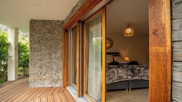 A room with a stone wall, wooden flooring, a bed with a patterned bedspread, and a hanging light fixture. - Wake to the Matterhorn in Luxury 1084 (Wallis)