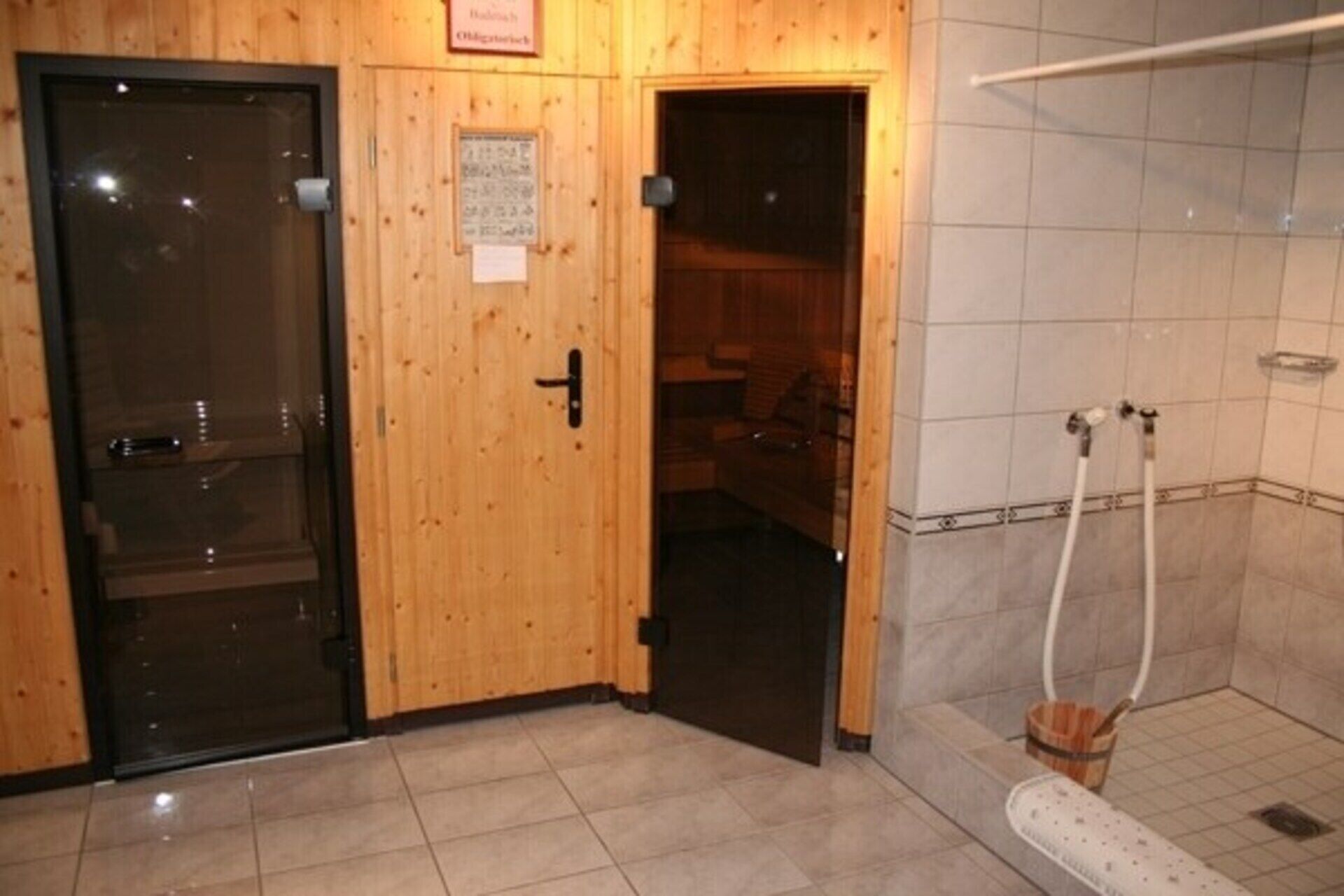 Une porte en bois avec une pancarte, un espace de douche carrelé et un pommeau de douche visible.