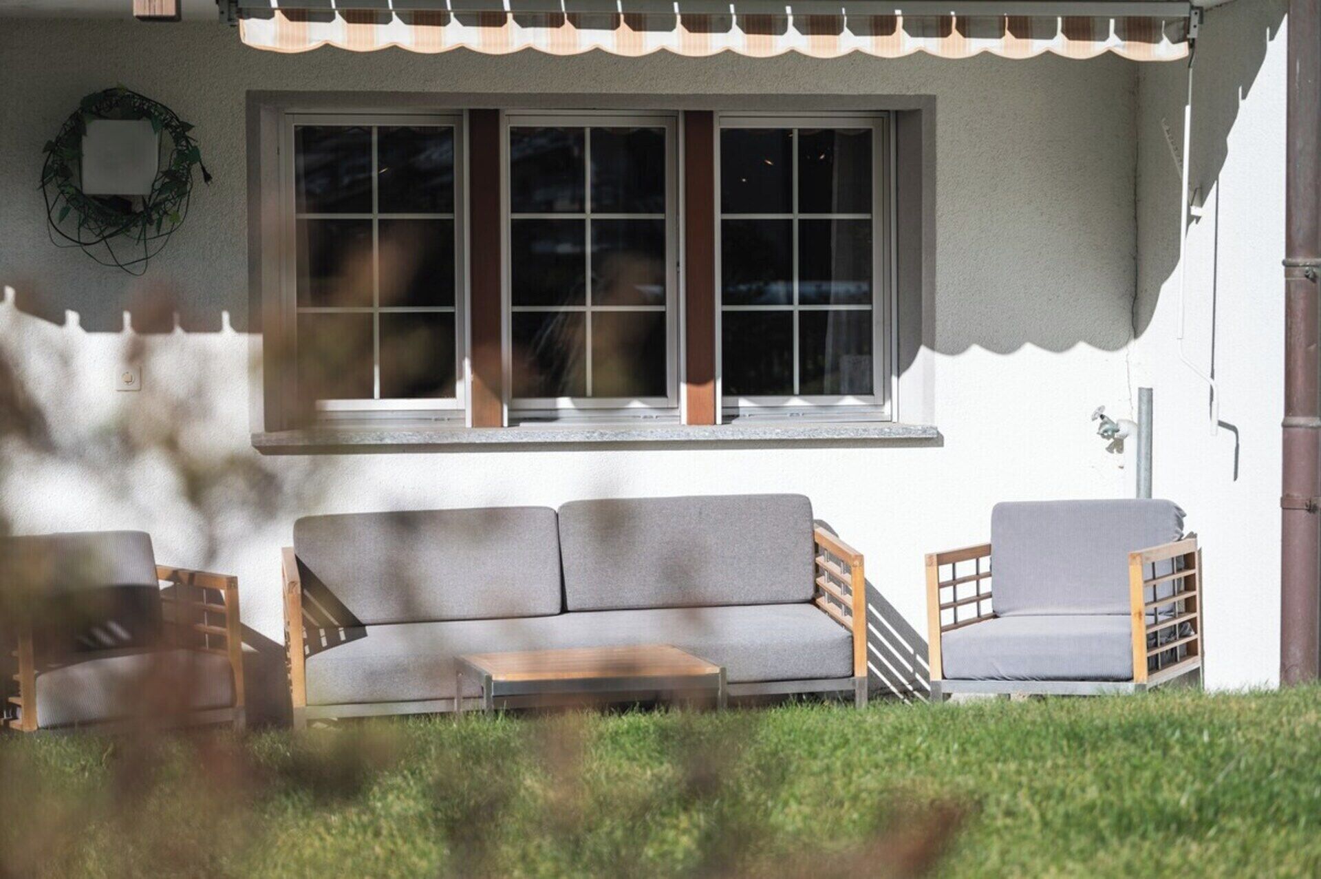 Une maison avec une véranda, un canapé gris, une chaise en bois et une petite table.