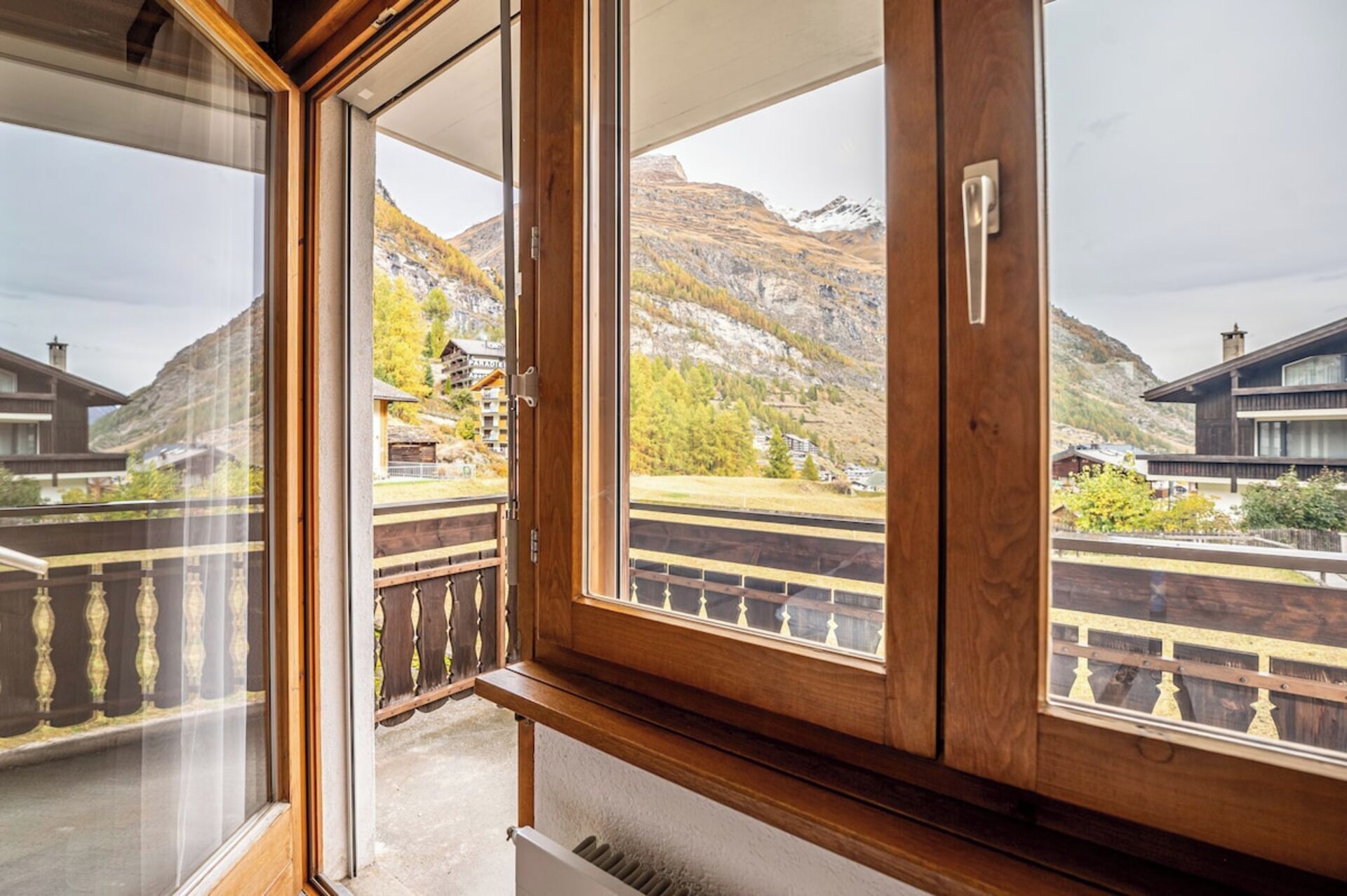 A room with a balcony overlooking a mountainous landscape with buildings.