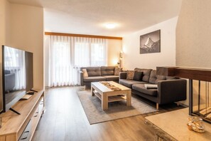 Ein modernes Wohnzimmer mit Flachbildfernseher, zwei Sofas, einem Couchtisch und einem großen Fenster mit durchsichtigen Vorhängen.