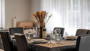 Uma mesa de jantar posta com cadeiras, uma garrafa de vinho e um vaso com flores secas.