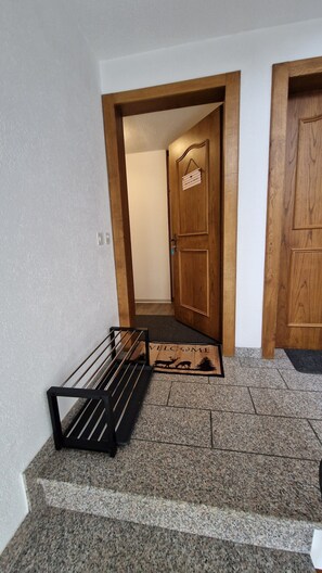 Un pasillo con una puerta de madera, un felpudo con siluetas de animales y un perchero metálico.