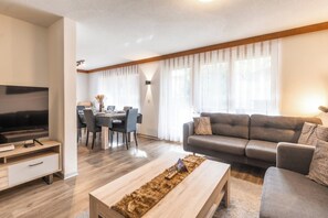 A modern living room with a flat-screen TV, a sofa, a coffee table, and a dining area with a table and chairs. - Where Alpine Luxury Meets the Matterhorn 1086 (Wallis)