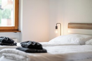 Ein ordentlich bezogenes Bett mit einem Holzkopfende, einer Nachttischlampe und einem Fenster mit Blick auf Grünflächen.