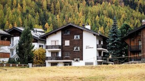 Um edifício em estilo chalé com varanda, emoldurado por uma paisagem montanhosa coberta por árvores.
