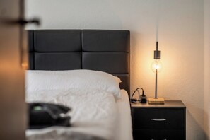 Un dormitorio con una cama, una mesita de noche con lámpara y otro mesita.