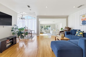 Uma sala de estar moderna com televisão de tela plana, um sofá azul e um espaço de jantar com lustre.