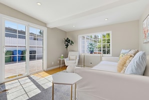 A modern living room with a sofa, a small table, and a chair. There are large windows with a view of the outside.