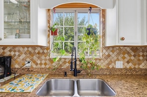 Uma cozinha com uma pia dupla, uma janela com plantas penduradas e painel de azulejos.