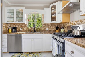 A modern kitchen with white cabinetry, a stainless steel dishwasher, a gas stove, and a window with a view of greenery. - Welcome to Casa Limón, a quiet, spacious home in Lake Balboa. (Los Angeles)