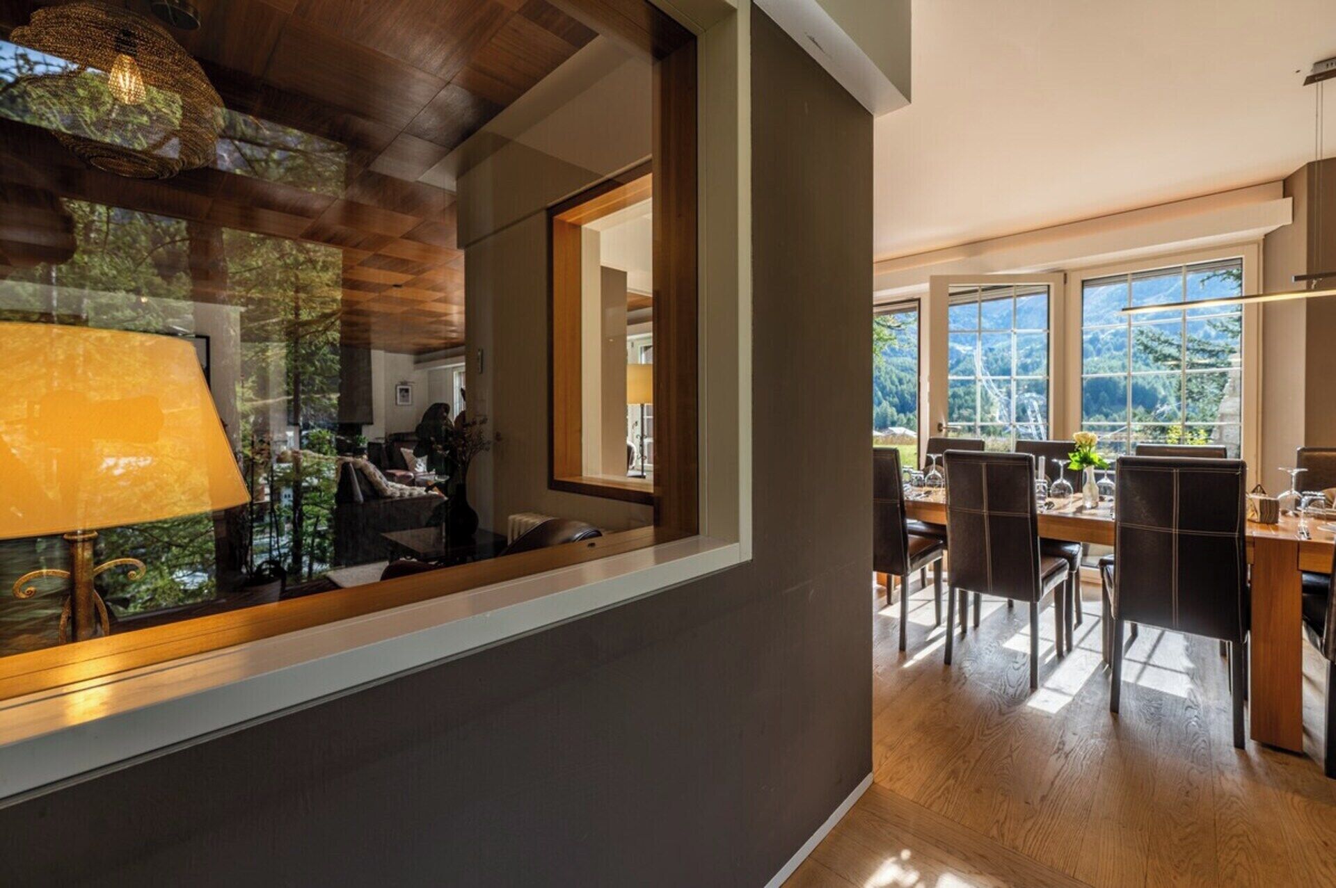 A modern interior with a dining area, large windows, and a view of greenery.