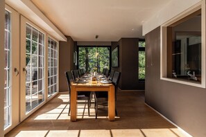 A dining area with a table set for four, large windows on one side, and a view of greenery outside.