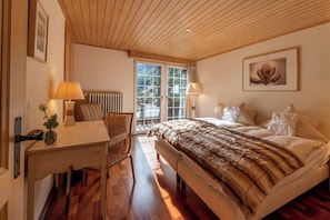 Et soveværelse med træloft, en seng med et pelslignende dække, et skrivebord med lampe og en stol.
