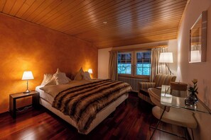 A hotel room with a wooden ceiling, a bed with a fur throw, a desk with a chair, and a window with curtains.