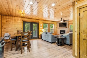 A wooden cabin interior with a dining area, sofa, fireplace, and a ceiling fan. - NEW! Modern Smokies Cabin! Hot Tub! Games! POOL! (Pigeon Forge)