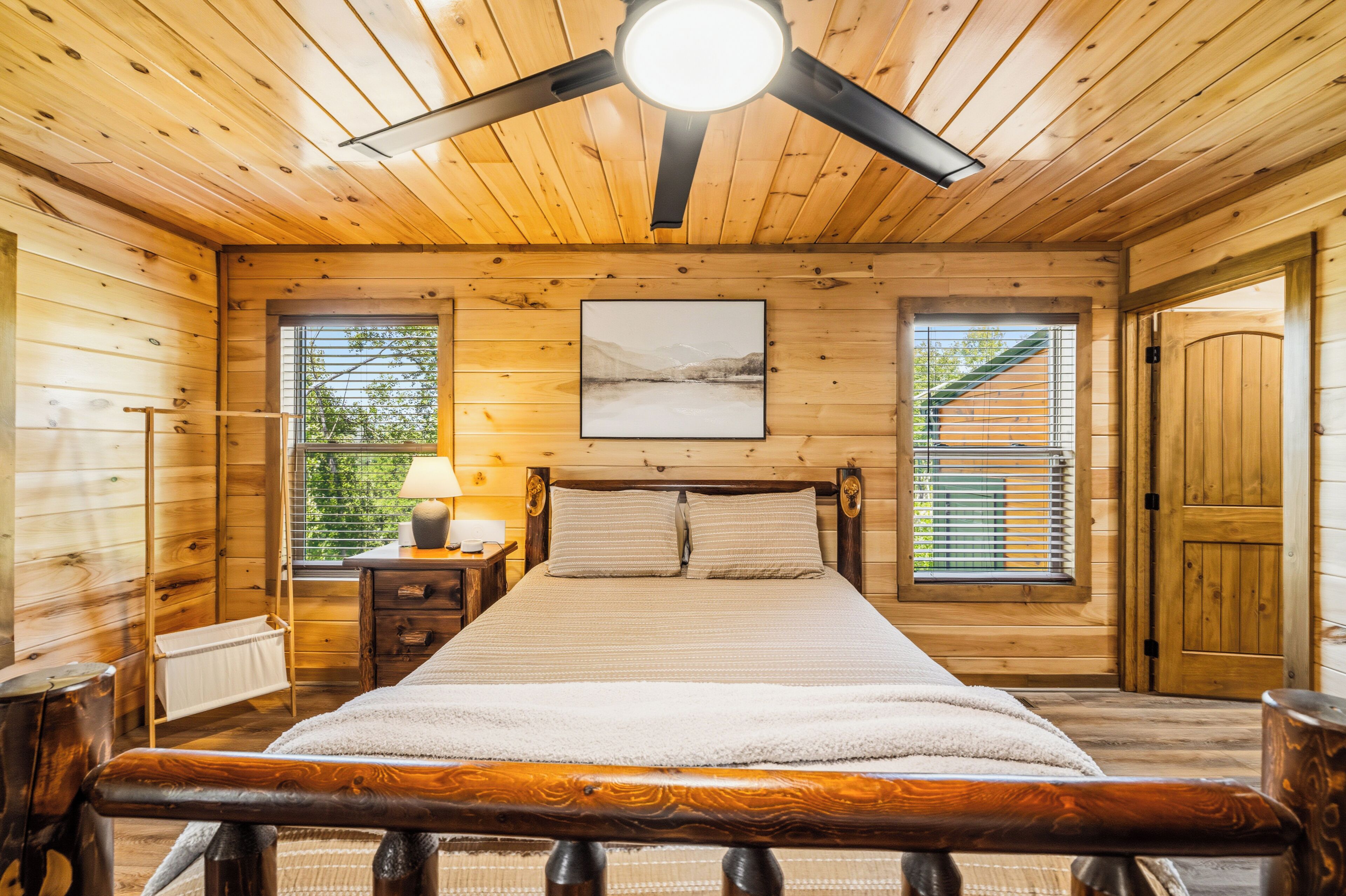 Ein Schlafzimmer in einer Holzhütte mit Bett, Nachttisch, Lampe und einem Bild an der Wand.