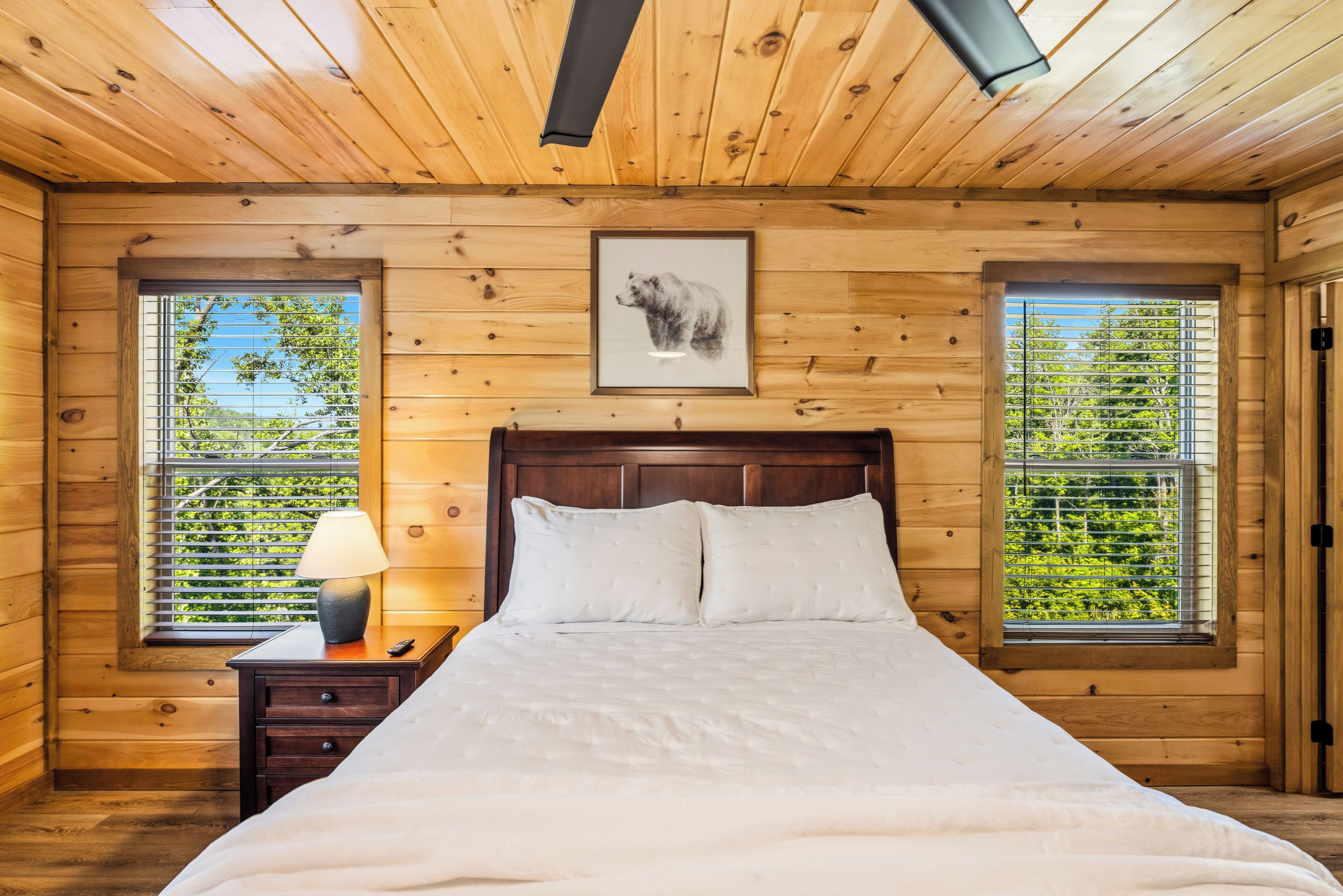 Une pièce en bois avec un lit, une table de chevet, une lampe et un tableau encadré au mur.