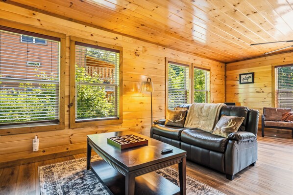 L’intérieur chaleureux d’un chalet avec un canapé en cuir, une table sur laquelle est posé un jeu de société et une lampe.