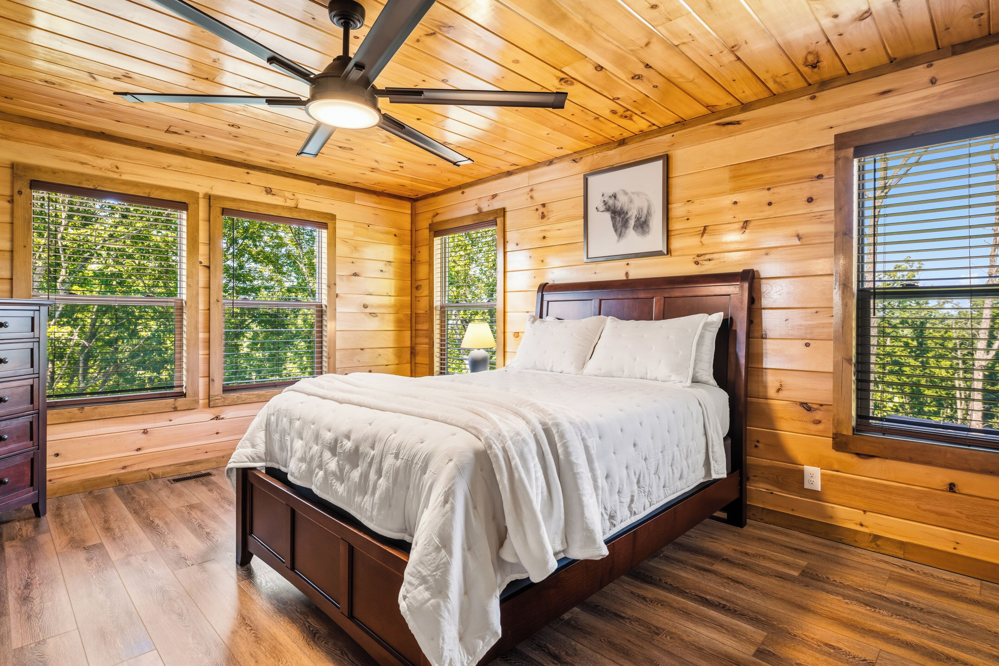 Ein Schlafzimmer mit Holzwänden, einem Bett, einem Deckenventilator und großen Fenstern.