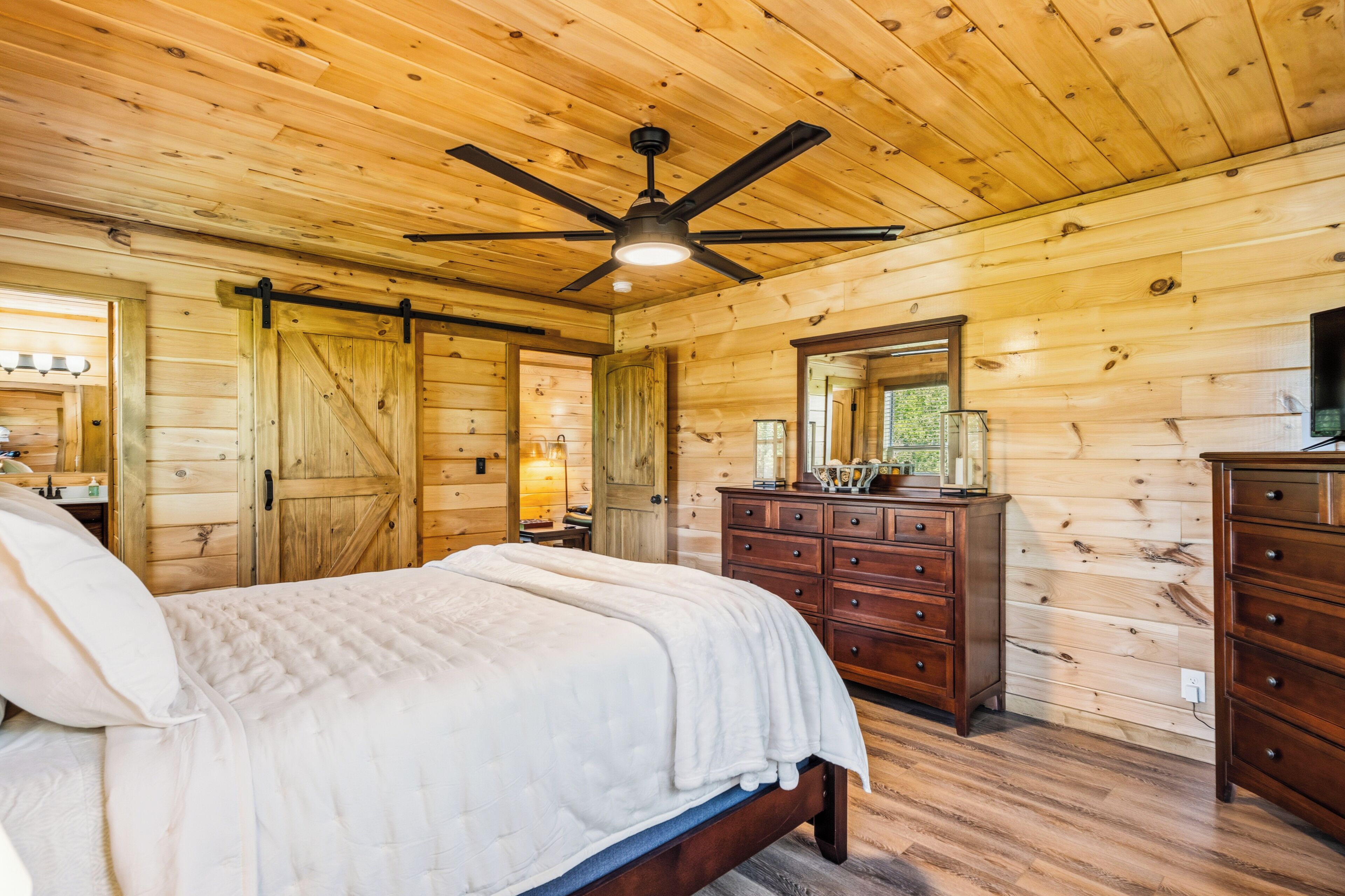 A wooden cabin bedroom with a bed, dresser, and a ceiling fan.