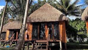 A thatched-roof bungalow with a wooden deck and a single chair outside.