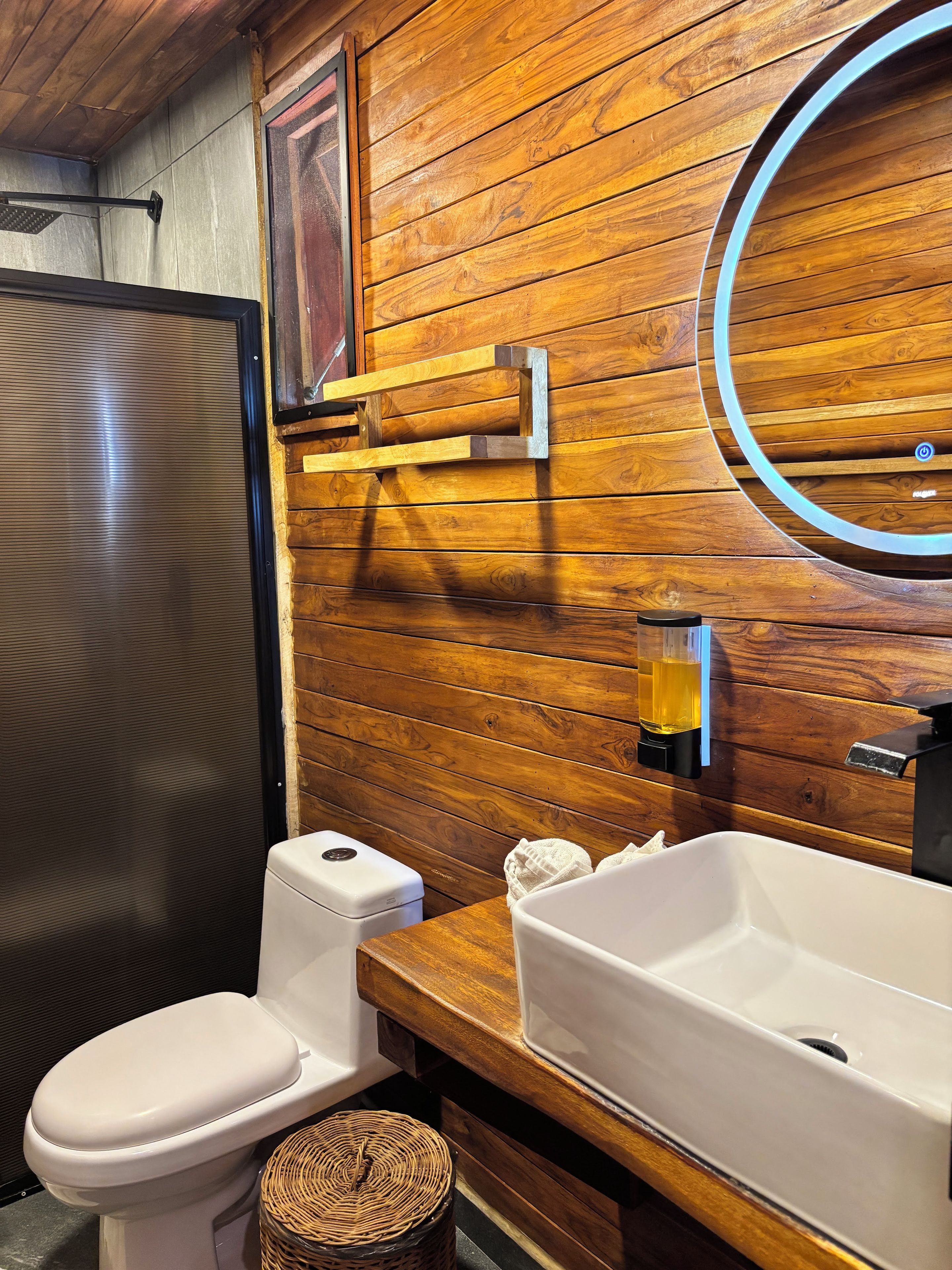 A bathroom with a wooden wall, a toilet, a sink, and a mirror.