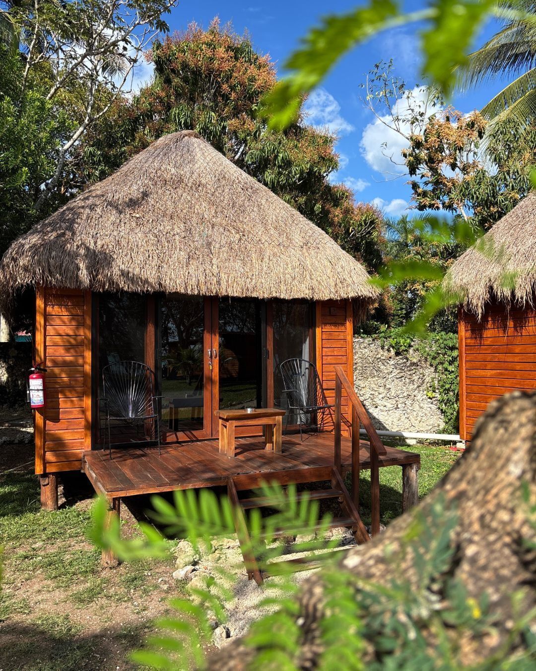 Una cabaña con techo de paja, un muelle de madera, asientos y un extintor.