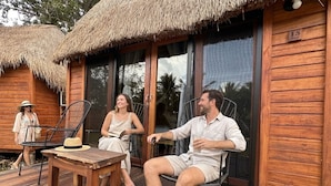 Eine Holzhütte mit einem Strohdach, einer Holzdiele und einer Glasdoor, die zu einem überdachten Außenbereich führt.